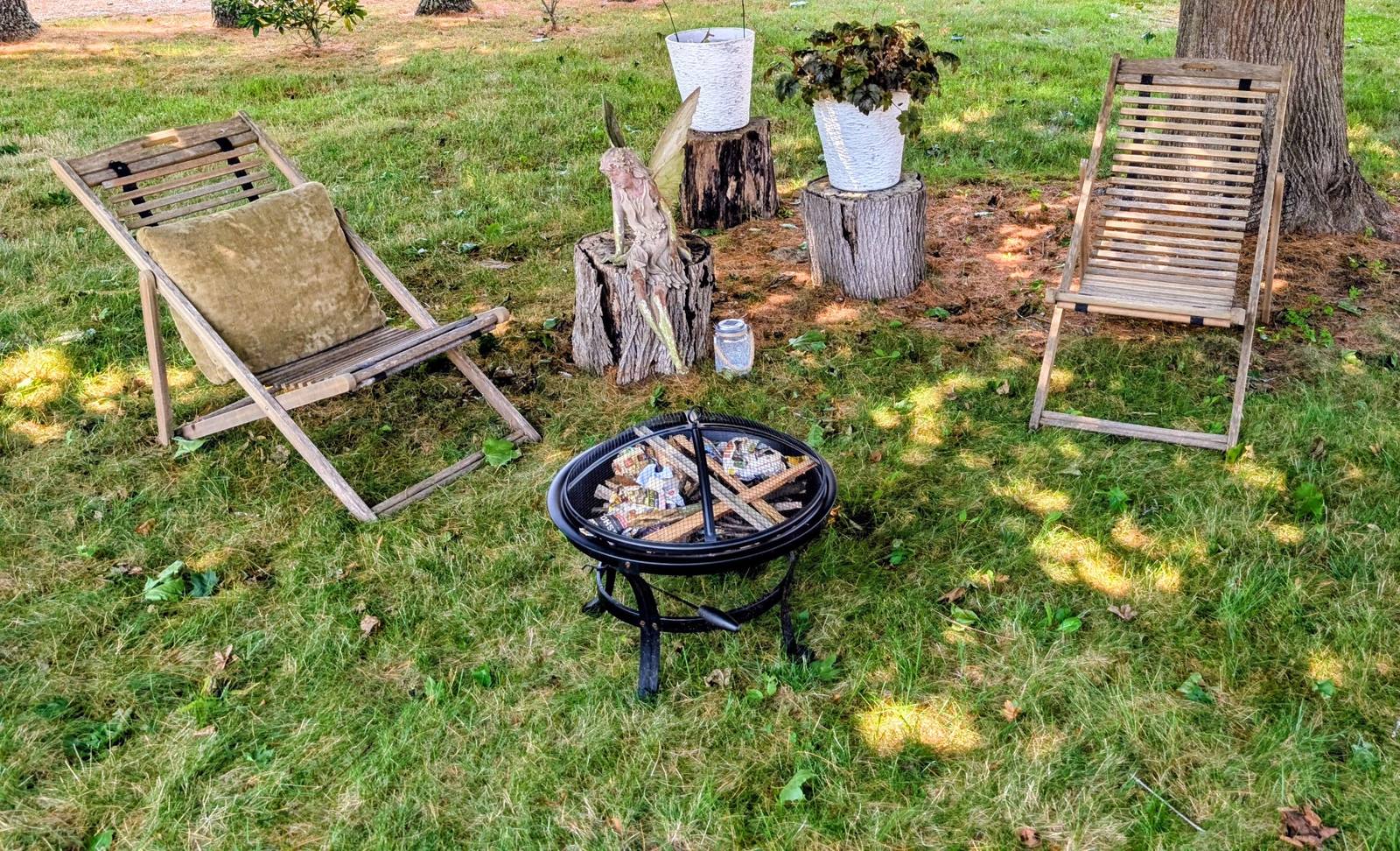 Two chairs gathered around the backyard fire pit under the trees